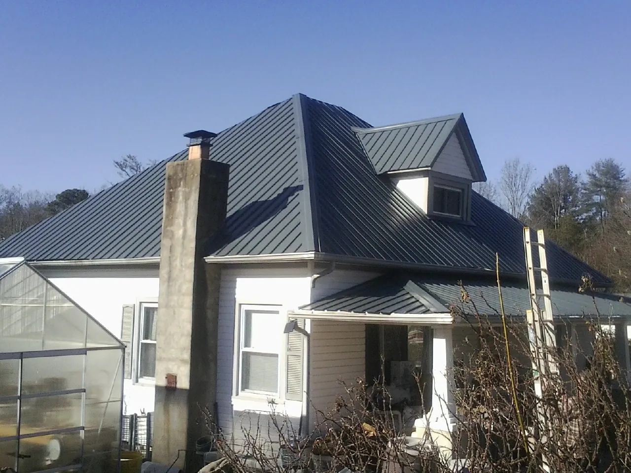 Dark blue standing seam metal roof on a white farmhouse with dormer — Slate & Tile Roof Repair by Roofing Brothers in Natrona Heights