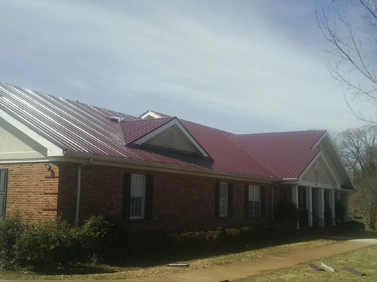 Red metal roof with gabled entries on a long brick building, from a Hail Damage Roof Repair job in Natrona Heights