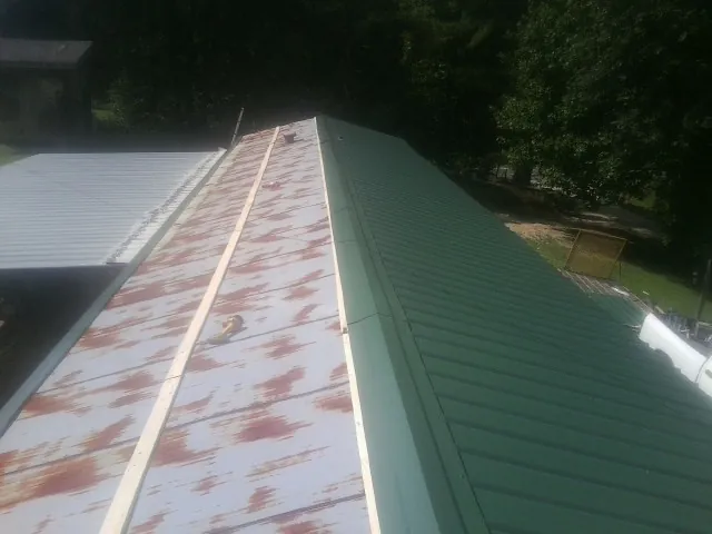 Old rusted panels beside newly installed green metal roofing — Wind Damage Roof Repair by Roofing Brothers in Natrona Heights