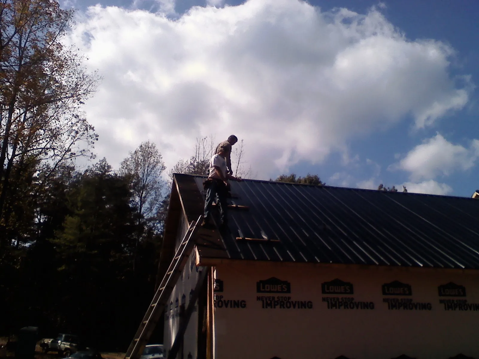 Roofer fastening dark metal panels high against a cloudy sky, from a Roof Inspection job in Natrona Heights