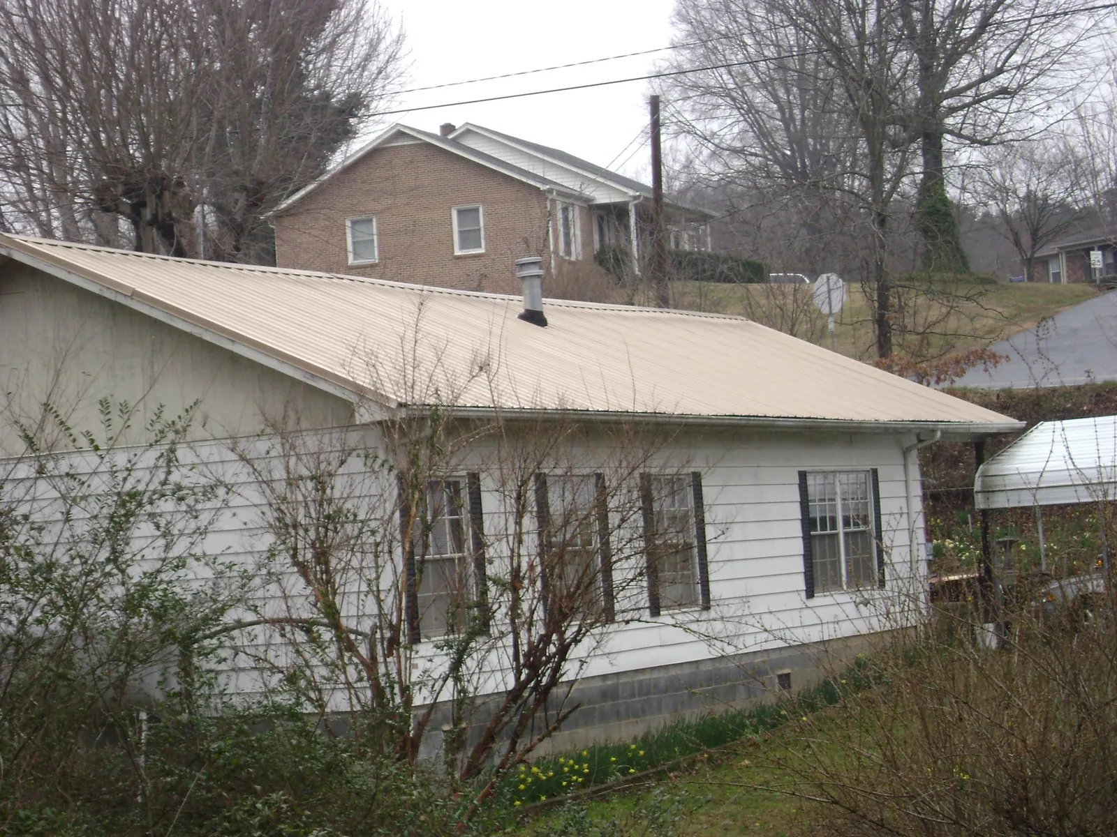 Tan metal roof on a white sided house set into a hillside — Commercial Roofing by Roofing Brothers in Natrona Heights
