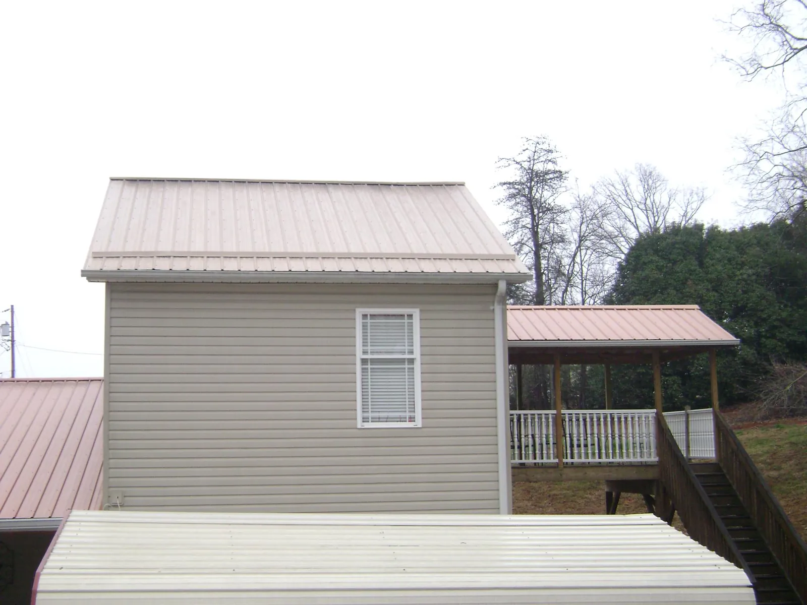Tan metal roofs on a two story addition and attached porch, from a Roof Replacement job in Natrona Heights